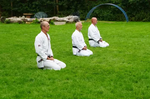 Drie senseis zitten in seiza op het gras