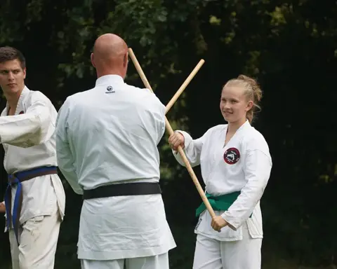 Sensei corrigeert een jonge karateka bij een staftechniek