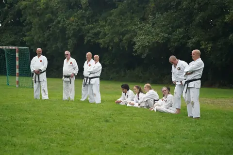 Karateka's oefenen in tweetallen terwijl anderen op het gras toekijken