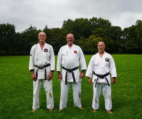 Drie senseis poseren samen op het grasveld