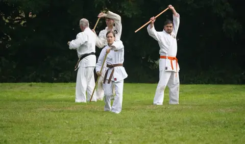 Karateka met oranje band oefent een techniek met de jo
