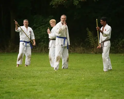 Karateka's trainen met jo-staf op het grasveld tijdens de weekendtraining
