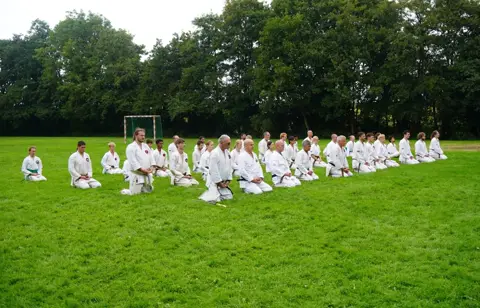 Deelnemers zitten op het gras en kijken naar een demonstratie