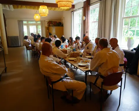 Karateka's eten samen aan lange tafels in het boshuis