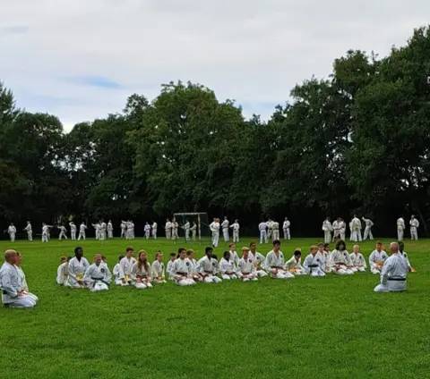 Deelnemers zitten in een kring op het gras tijdens een uitleg