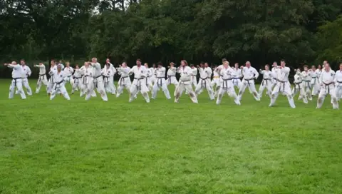 Grote groep karateka's traint basistechnieken in lange rijen op het grasveld