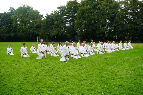 Groep zit in seiza op het veld aan het begin van de les