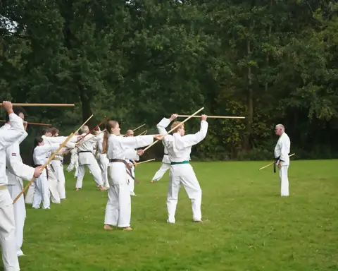 Grote groep oefent jo-technieken onder leiding van de sensei