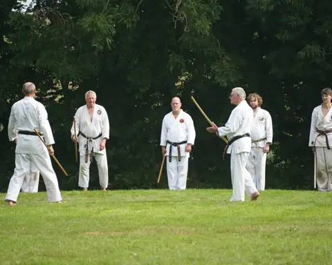 Rij karateka's oefent jo-technieken op het gras