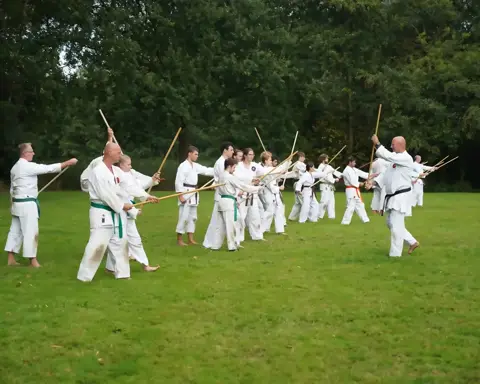 Twee rijen karateka's oefenen jo-technieken tegenover elkaar