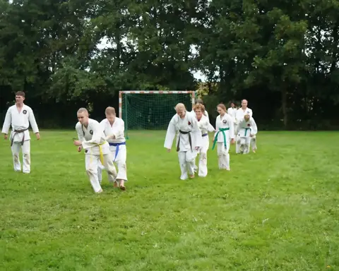 Karateka's rennen als warming-up over het grasveld