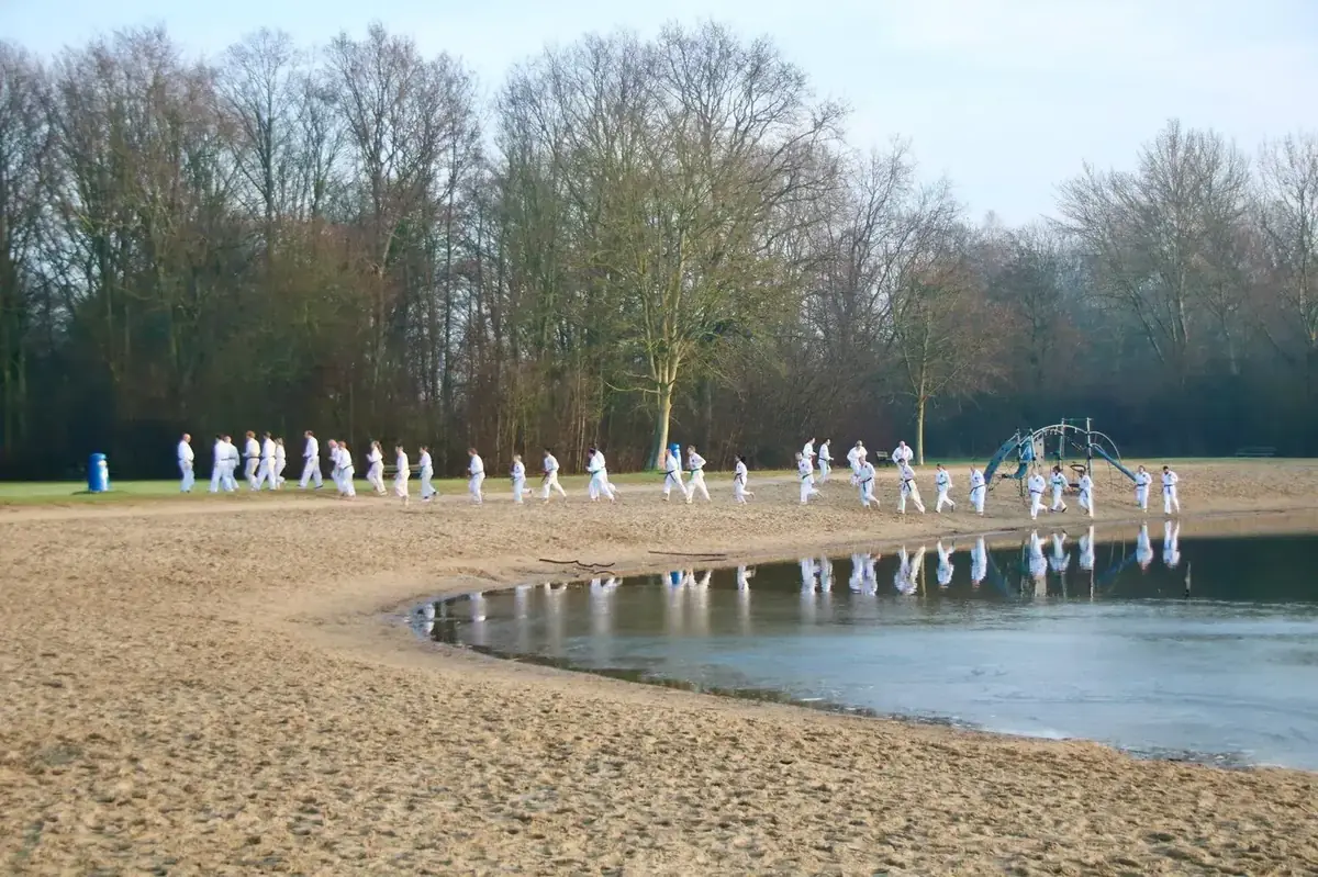 Karategroep loopt langs het bevroren meer in het Streekbos