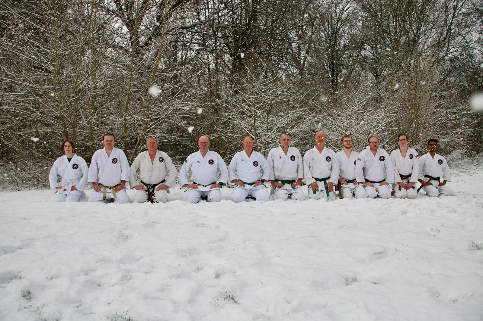 Karateleerlingen zitten in seiza-houding in de sneeuw, in rij naast elkaar met vallende sneeuwvlokken